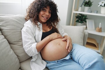 Pregnant woman smile and happiness lies on the couch freedom and strokes her belly with a baby in the last month of pregnancy, mother's day lifestyle