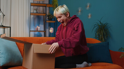 Happy surprised winner woman unpacking delivery parcel at home. Smiling satisfied girl shopper...