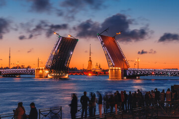 White nights in St. Petersburg. Divorced Palace Bridge and Peter and Paul Fortress at dawn. People look at the St. Petersburg dawn on the Neva.