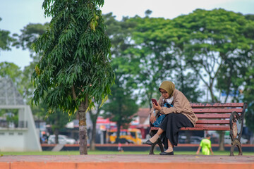 Fototapeta na wymiar Woman sitting alone on a park bench in Kutoarjo, 5 February 2023