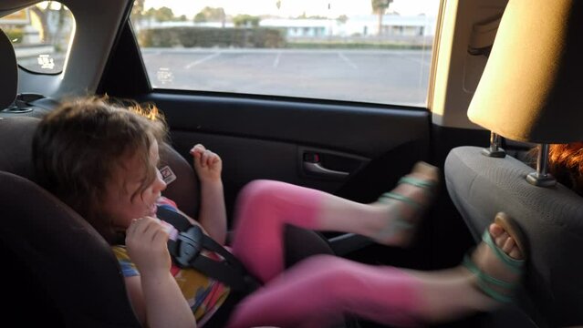 Handheld shot of playful daughter hitting on mother's seat while sitting in car