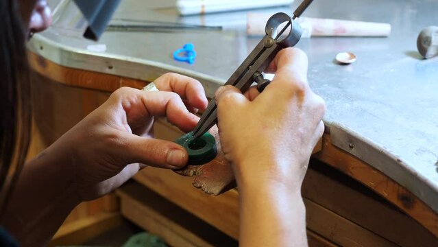 Handheld shot of female jeweller using drawing compass for marking on wax in workshop