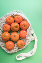 A cotton mesh grocery shopping bag reusable with tangerines on green background