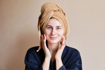 woman in a robe and with a towel on her head applies cosmetics to skin