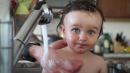 Baby boy getting cleaned in kitchen skink