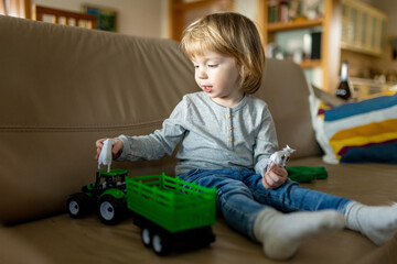 Cute toddler boy playing with green toy tractor at home.