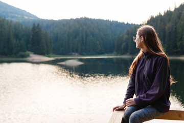 Fototapeta premium female tourist in a sweater and jeans near a mountain forest lake