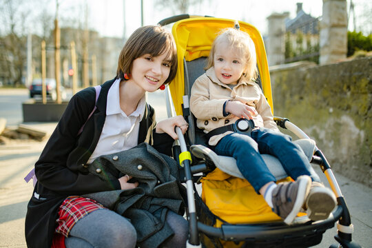 Older sister and her toddler brother sitting in a stroller outdoors. Infant kid in pushchair. Spring walks with kids.