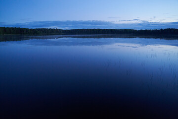 Evening landscape with a lake and forest mirroring in water.