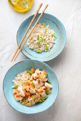 Turquoise bowls with korean chicken and kimchi stir-fry, above view on a beige stone background, vertical shot