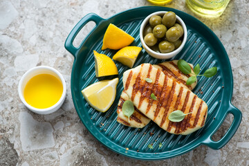 Green serving tray with bbq halloumi, olives and lemon, elevated view on a brown granite background, horizontal shot
