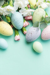 Easter colored eggs and a bouquet of white and pink carnations with eucalyptus branches on a soft green background.