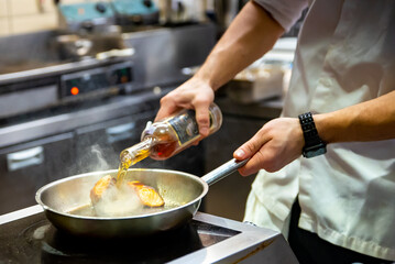 man chef cooking fried salmon fish in frying pan on kitchen