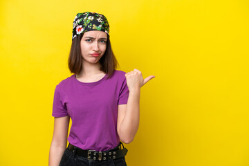 Young Ukrainian woman isolated on yellow background unhappy and pointing to the side
