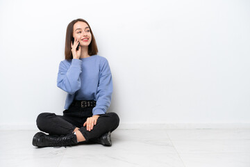 Fototapeta na wymiar Young Ukrainian woman sitting on the floor isolated on white background keeping a conversation with the mobile phone with someone