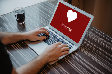 Hand typing a computer laptop and heart screen with red background on the wooden table. Find or choose love couple concept. Valentine day.