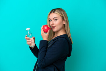 Young caucasian woman isolated on blue background with an apple and with a bottle of water