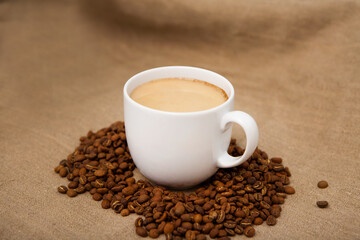coffee cup with roasted beans. Cappuccino with milk white mug, coffee beans. brown fabric background