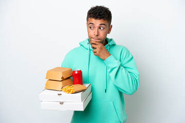 Young Brazilian holding fast food isolated on white background having doubts and thinking