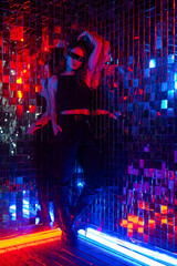 Fototapeta premium Portrait of a caucasian woman in sunglasses in neon light against a mirror wall. 