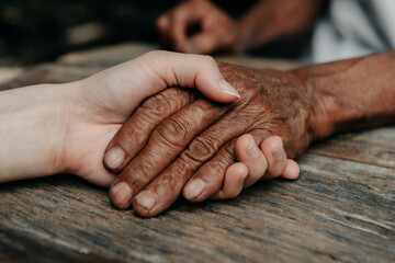 Hands of the old man and a woman hand on the wood table in sun light.