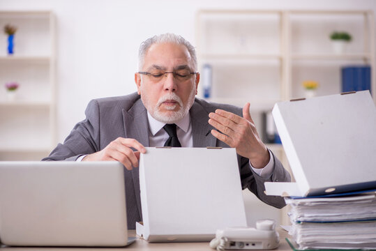 Old male employee eating pizza in the office - Powered by Adobe