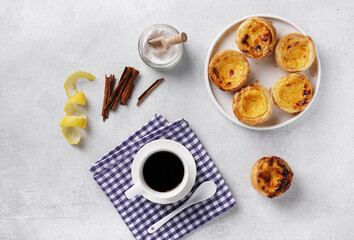 Pastel de nata. Traditional Portuguese dessert, egg tarts over cobcrete background with cinnamon sticks and cup of coffee decorated with blue napkin. Top view