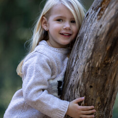 Smiling blonde little girl leaning on fallen tree