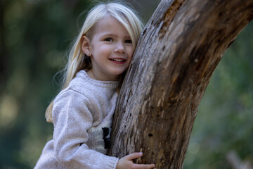 Smiling blonde little girl leaning on fallen tree