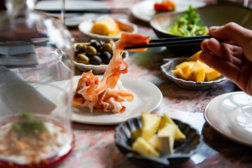 man hand eating prosciutto in restaurant. wine, cheese, meat, vegetables and other appetizers on table