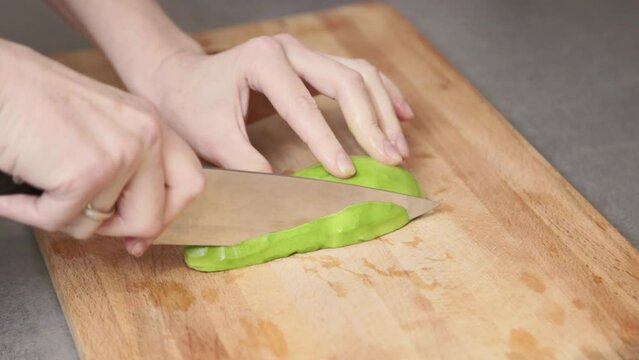 A woman cuts an avocado on a wooden cutting board in the kitchen. Vegan breakfast snack. Video in slow motion.