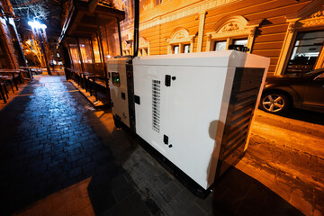 Large stationary diesel power three phase electric silent generator set in evening city.