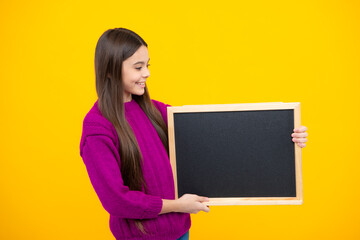 Teenage girl child holding blackboard, isolated on a yellow background.