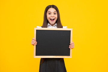 Teenage girl child holding blackboard, isolated on a yellow background. Excited face, cheerful emotions of teenager girl.