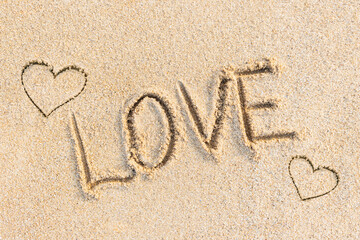Love word and heart signs written on textured sand surface