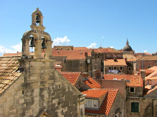 A view of Dubrovnik Croatia's famous orange terra cotta colored roofs on a bright sunny day, with a view of a church tower with bells in the foreground.  Image has copy space.