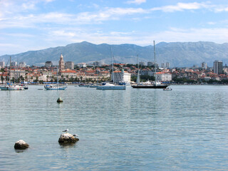 Boats off the coast of Split, Croatia with the city and mountains behind them on a sunny day with a blue, cloudy sky.  Image has copy space.