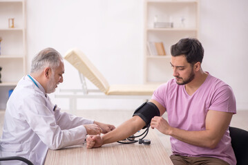 Obraz premium Old male doctor measuring young patient's blood pressure