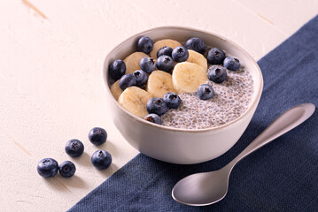 Chia pudding with fresh blueberries and banana on a white wooden surface with dark blue linen; copy space