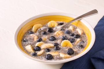 Chia pudding with fresh blueberries and banana in a yellow bowl on a white wooden surface; copy space