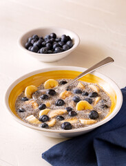 Plant based breakfast of fiber rich chia pudding with blueberries and banana in a yellow bowl on a white wooden surface; copy space