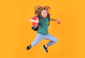 Kid jump and enjoy school. Funny child school boy jumping on a yellow studio background.
