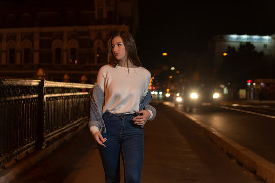 Attractive young woman walking on night street. Stylish girl in white t-shirt, evening city street background