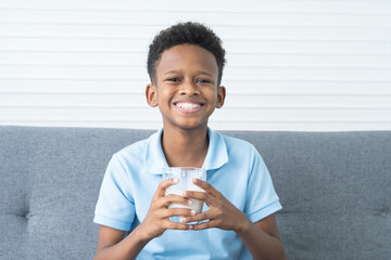 Portrait of adorable African Nigerian boy smiling with milk moustache, holding and drinking a glass...