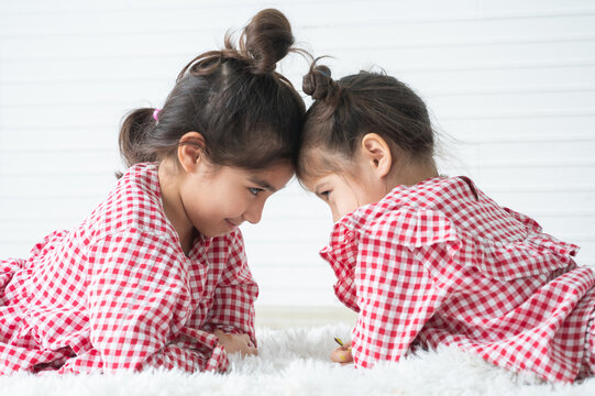 Little cute siblings, Asian, children girls playing bump each other head, lying on white fluffy carpet on floor together at home. Family relationship and lifestyle concept