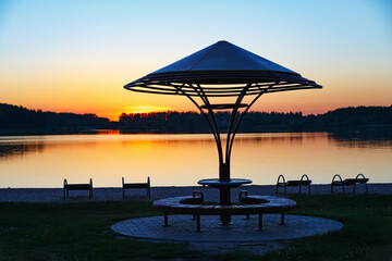 Bench with a canopy on the background of the lake and the sunset sky. Place for rest.