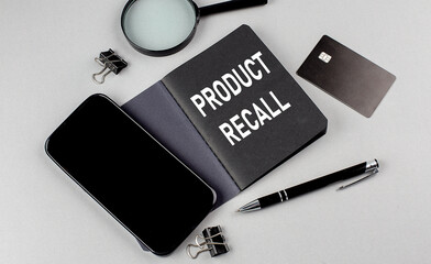 PRODUCT RECALL text written on black notebook with smartphone, magnifier and credit card