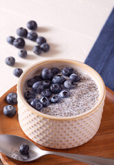 Fototapeta na wymiar Fiber rich chia pudding with fresh blueberries on a white wooden surface with dark blue linen; copy space
