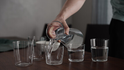Fototapeta na wymiar Man pour water into glasses from carafe on walnut table