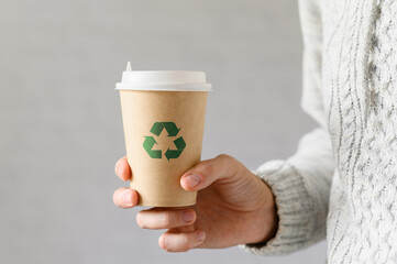 Disposable paper cup with recycling sign in hand. The concept of zero waste